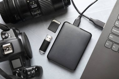 Diz üstü bilgisayara, hafıza kartına, flash diske, kameraya ve lense bağlı harici sabit disk gri desenli tabloda düz konum