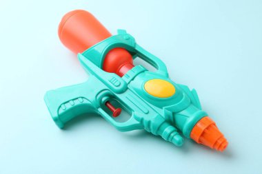 Açık mavi arkaplanda parlak plastik su tabancası, yakın plan.