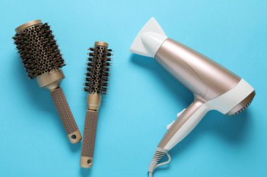 Açık mavi arkaplanda saç kurutma makinesi ve fırçalar, düz konum