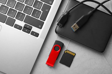 Flaş bellek, hafıza kartı, harici hard disk ve dizüstü bilgisayar açık gri tabloda, düz konum
