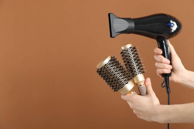 Saç kurutma makinesi ve kahverengi arka planda yuvarlak fırçalı bir kadın, yakın plan. Metin için boşluk
