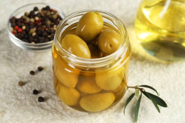 Kavanozda turşulu yeşil zeytin, beyaz desenli masada yağlı ve biberli mısır, yakın plan.