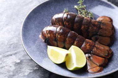Çiğ ıstakoz kuyruğu, kireç ve kekik karanlık masada, yakın plan.