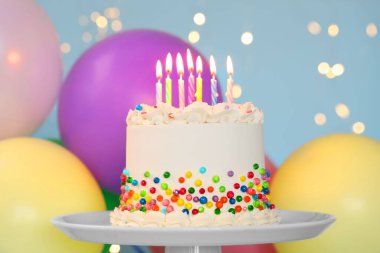 Renkli serpilmiş nefis bento keki ve açık mavi arka planda yanan mumlar bulanık ışıklara karşı, yakın plan