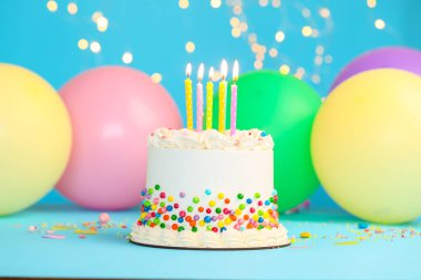 Renkli serpilmiş nefis bento keki ve bulanık ışıklara karşı açık mavi masada yanan mumlar.