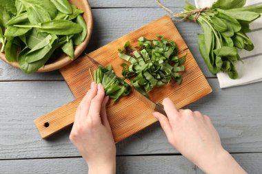 Gri ahşap masada taze kuş yaprakları kesen kadın.