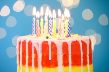 Açık mavi arkaplanda yanan mumlarla enfes bir doğum günü pastası, bulanık ışıklar, yakın plan.