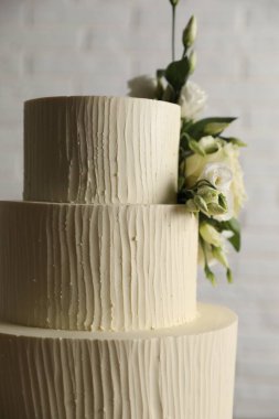 Bulanık beyaz arka planda çiçeklerle süslenmiş lezzetli düğün pastası.