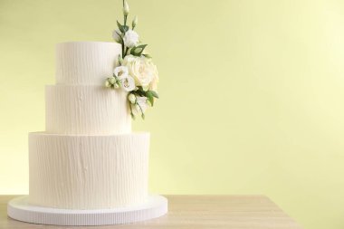 Ahşap masadaki çiçeklerle süslenmiş nefis bir düğün pastası açık yeşil arka planda, yakın plan. Metin için boşluk