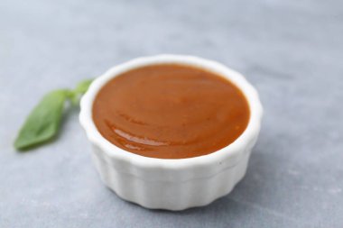 Lezzetli köri sosu ve fesleğen yaprakları gri masada, yakın plan.