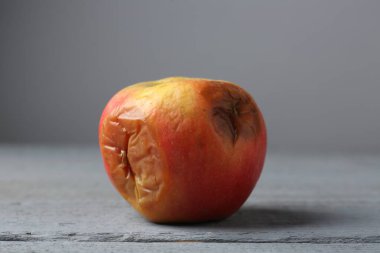 Gri ahşap masada çürük bir elma, yakın plan.