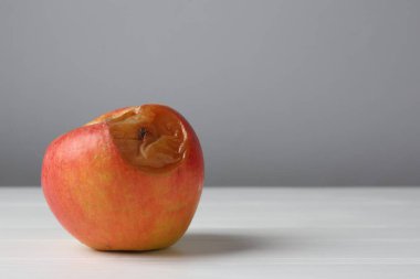 Beyaz ahşap masada gri arka planda çürük bir elma, yakın plan. Metin için boşluk
