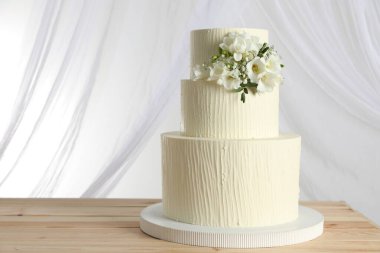 Ahşap masadaki çiçek desenli nefis düğün pastası ve beyaz arka plandaki perdeler.