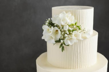 Gri arka planda çiçek dekoru olan lezzetli düğün pastası, yakın plan. Metin için boşluk