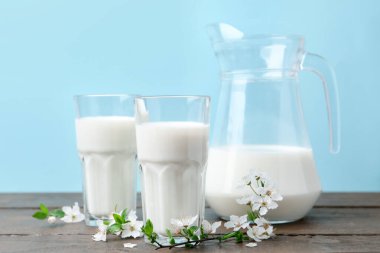 Taze süt ve çiçekler beyaz masada açık mavi arka planda