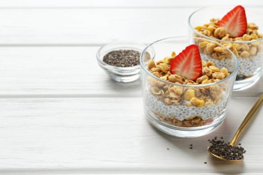 Beyaz ahşap masadaki bardaklarda Chia tohumları, yoğurt, granola ve çilek ile nefis bir tatlı, yazı için yeri olan yakın plan. Süper yemek.