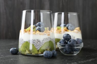 Chia tohumlu lezzetli tatlı, yoğurt, granola, yaban mersini ve kivi siyah masada, yakın plan. Süper yemek.