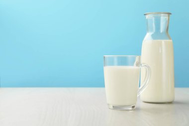 Fincanda taze süt ve açık mavi arka planda beyaz ahşap masada sürahi. Metin için boşluk