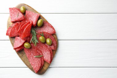 Beyaz ahşap masada servis edilen zeytinli ve biberiyeli leziz sosis dilimleri. Metin için boşluk