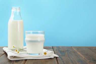 Taze süt ve çiçekler ahşap masada açık mavi arka planda, yakın plan. Metin için boşluk