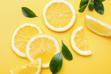 Sarı arka planda taze limon ve yeşil yapraklar var.