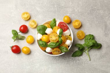 Sarı domatesli taze salata, fesleğen ve mozzarella peyniri gri masada, düz yerde.
