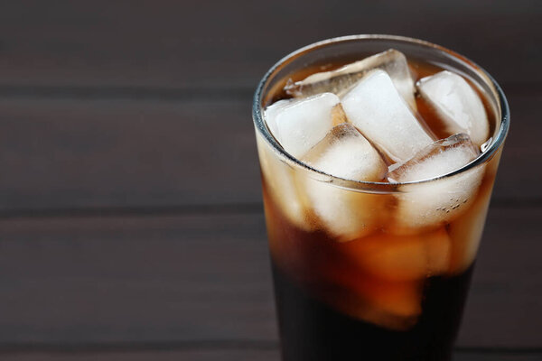 Refreshing cola with ice cubes in glass on wooden table, closeup. Space for text