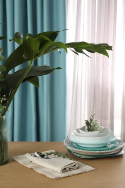 Pencerenin yanındaki ahşap masada zarif perdeleri olan bulaşık takımı