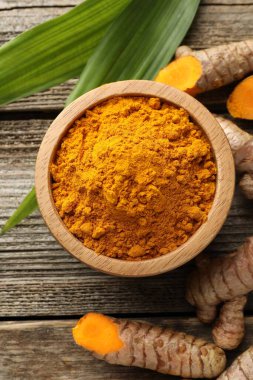 Tabaktaki zerdeçal tozu, kökler ve yapraklar ahşap masada, düz yerde.