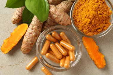 Zerdeçal kapsülleri, toz, kökler ve yeşil yapraklar gri masada, düz yerde.