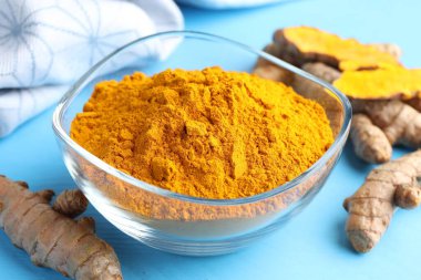 Kasede Aromatik zerdeçal tozu ve açık mavi ahşap masa üzerinde taze kökler, yakın plan.