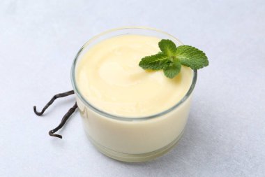 Lezzetli vanilyalı puding, nane ve kapsüller açık gri masada, yakın plan.