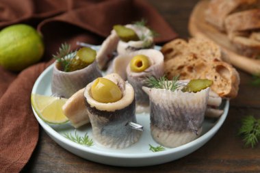 Lezzetli ringa dürümleri zeytin, turşu, dereotu ve ekmek parçaları ahşap masada, yakın plan.