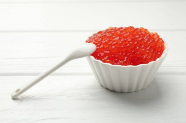 Lezzetli kırmızı havyar kasede ve kaşık beyaz ahşap masada, yakın plan