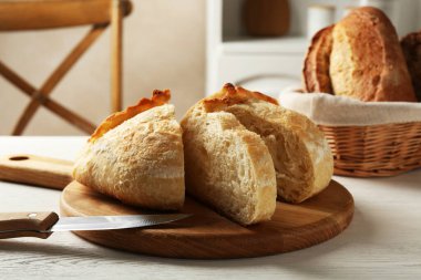Taze pişmiş ekmek ve bıçağı beyaz ahşap masada kes, yakın plan.