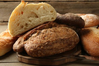 Tahta masada farklı somun taze ekmek ve bıçak, yakın plan.
