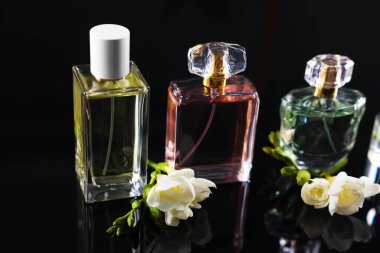 Siyah ayna yüzeyinde aromatik parfüm şişeleri ve çiçekler, yakın plan.