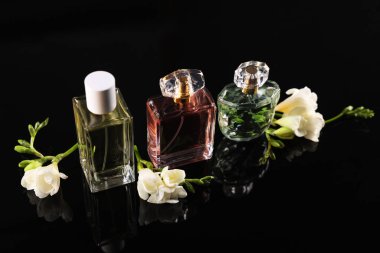 Siyah ayna yüzeyinde aromatik parfüm şişeleri ve çiçekler