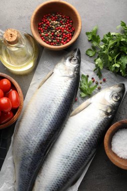 Tuzlu ringa balıkları, baharatlar ve domatesler gri masada, düz yerde.