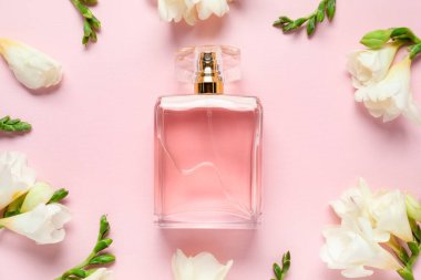 Bir şişe parfüm ve pembe arka planda güzel çiçekler.