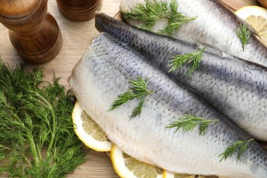 Ahşap masada dereotu ve limon dilimli lezzetli ringa filetoları, yakın plan.