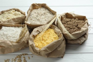 Beyaz ahşap masadaki kağıt torbalarda farklı türde un, yakın plan.