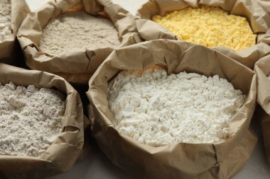 Beyaz masadaki kağıt torbalarda farklı türde un, yakın plan.