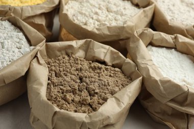 Beyaz masadaki kağıt torbalarda farklı türde un, yakın plan.