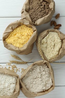 Beyaz ahşap masa üzerinde kağıt torbalarda farklı türde un, düz yerde.