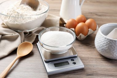 Tahta masadaki diğer ürünler arasında bir kase şekerli dijital mutfak terazisi.