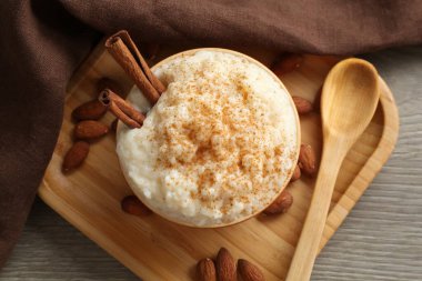 Tarçınlı, bademli, ahşap masadaki kaşıklı lezzetli sütlaç.