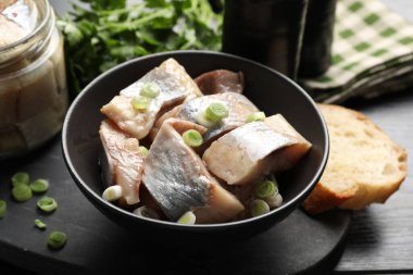 Siyah ahşap masada yeşil soğanlı lezzetli ringa balıkları, yakın plan.