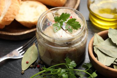 Kavanozda baharat ve siyah masada ekmek olan lezzetli ringa balıkları.