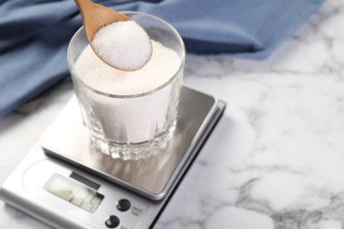 Beyaz mermer masadaki dijital mutfak terazisine şeker koymak, yakın plan. Metin için boşluk